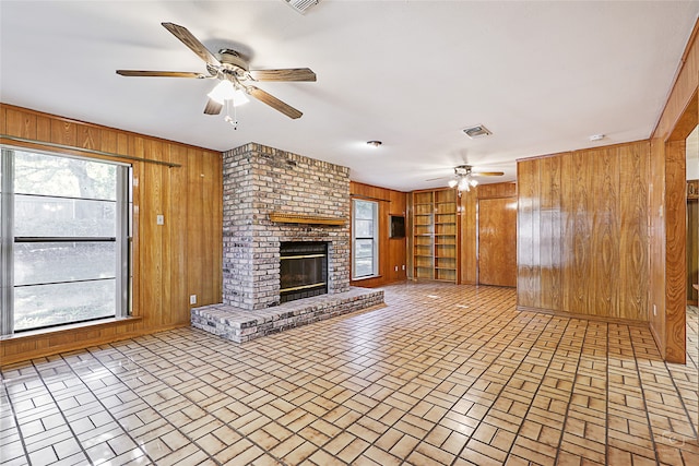 unfurnished living room with ceiling fan, built in features, wooden walls, and a brick fireplace