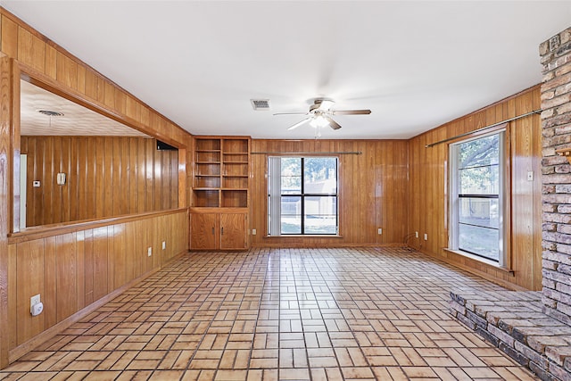 unfurnished living room featuring ceiling fan, plenty of natural light, and wood walls