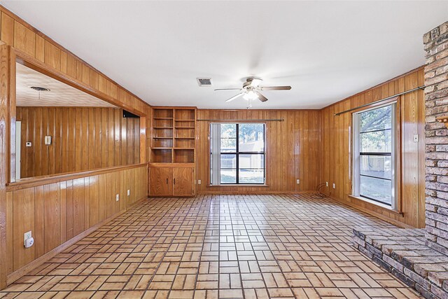 unfurnished living room featuring ceiling fan, plenty of natural light, and wood walls