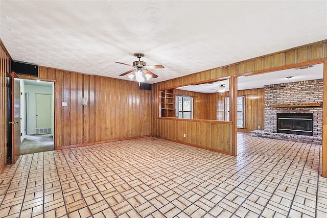 unfurnished living room featuring wood walls, a fireplace, and ceiling fan