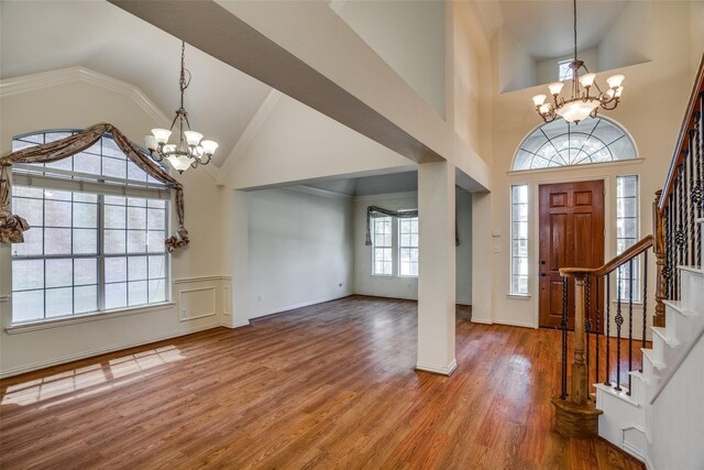 entrance foyer with wood-type flooring, crown molding, high vaulted ceiling, and a chandelier