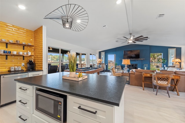 kitchen with appliances with stainless steel finishes, white cabinetry, lofted ceiling, and wood walls