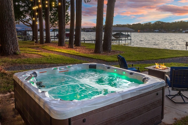 pool at dusk with a lawn, cooling unit, a water view, and a hot tub