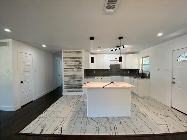 kitchen with white cabinetry, a center island, decorative light fixtures, decorative backsplash, and light wood-type flooring