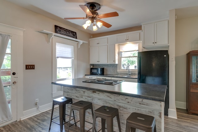 kitchen with decorative backsplash, white cabinets, black appliances, and wood-type flooring