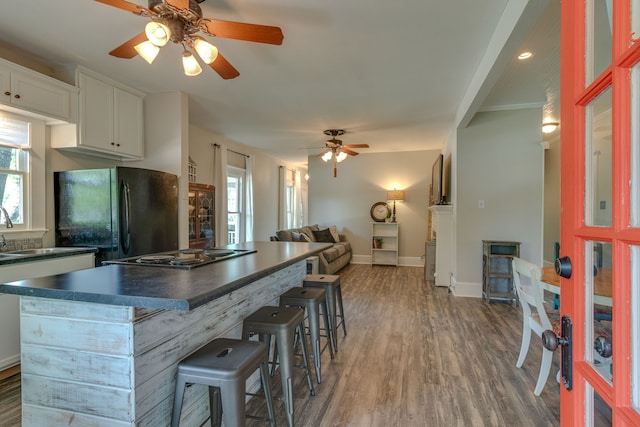 kitchen with white cabinetry, ceiling fan, a kitchen breakfast bar, dark hardwood / wood-style floors, and black appliances