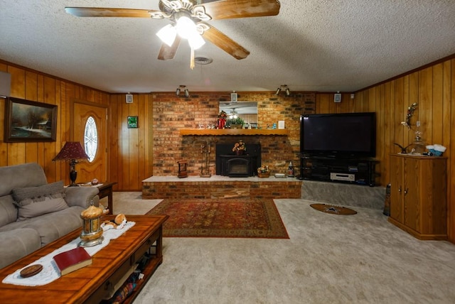 carpeted living room with ceiling fan, wood walls, a wood stove, and a textured ceiling