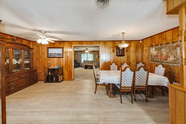 dining space with light wood-type flooring, a textured ceiling, ceiling fan, and wood walls