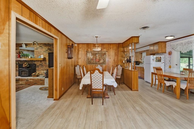 dining space featuring wood walls, a wood stove, crown molding, light wood-type flooring, and a textured ceiling