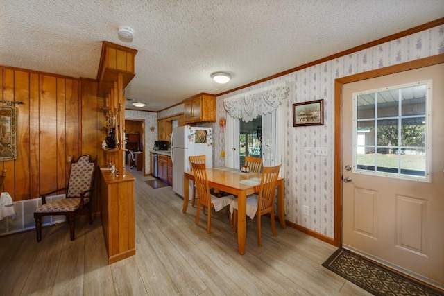 dining area with a textured ceiling, light wood-type flooring, ornamental molding, and wood walls