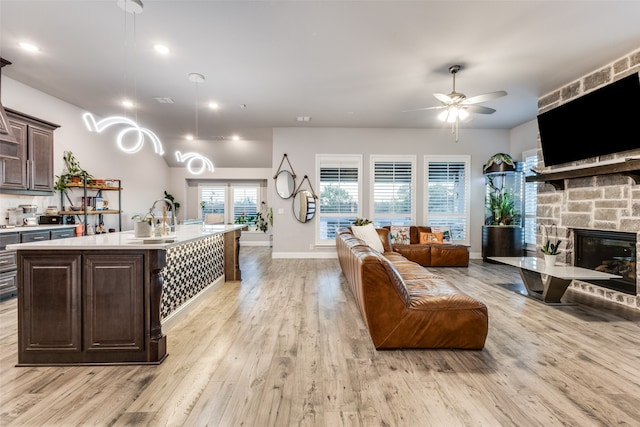 living room featuring a stone fireplace, ceiling fan, light hardwood / wood-style flooring, and sink