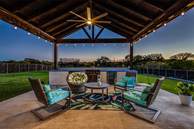 patio terrace at dusk featuring ceiling fan, a yard, and wine cooler