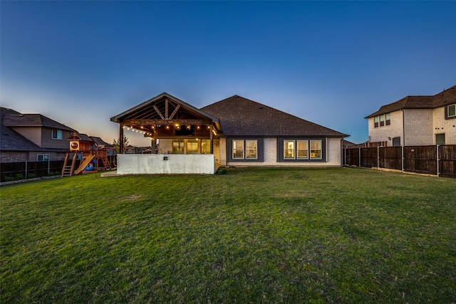 back house at dusk featuring a playground and a lawn