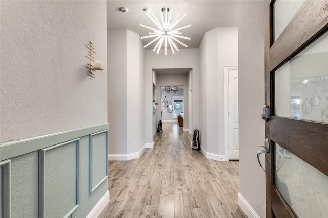 hall with light wood-type flooring and a notable chandelier