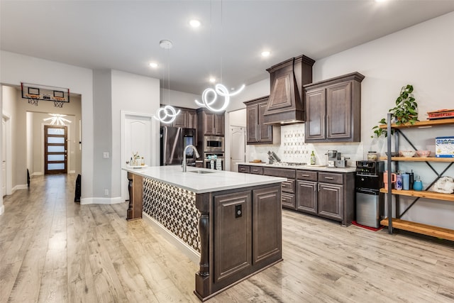 kitchen featuring dark brown cabinets, stainless steel appliances, sink, a center island with sink, and light hardwood / wood-style floors