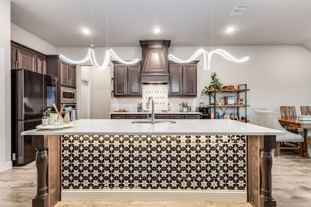 kitchen with stainless steel microwave, light hardwood / wood-style flooring, black fridge, and hanging light fixtures