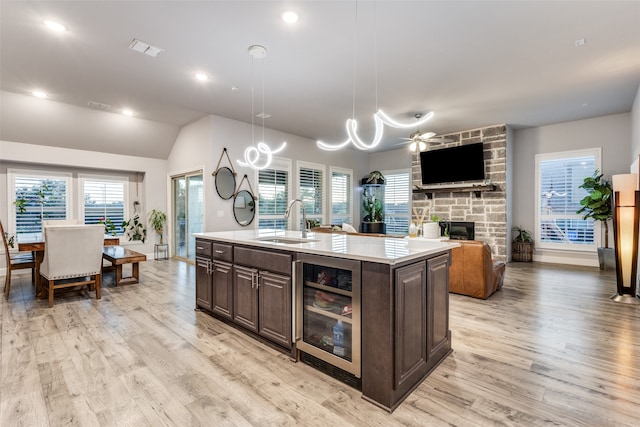 kitchen featuring a center island with sink, hanging light fixtures, sink, wine cooler, and light wood-type flooring