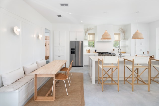 kitchen with appliances with stainless steel finishes, a kitchen island with sink, pendant lighting, white cabinetry, and a breakfast bar area