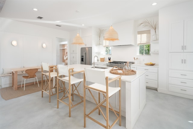 kitchen with white cabinets, high end refrigerator, sink, and an island with sink