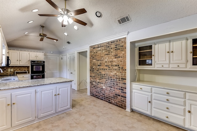 kitchen with lofted ceiling, sink, black double oven, ceiling fan, and white cabinetry