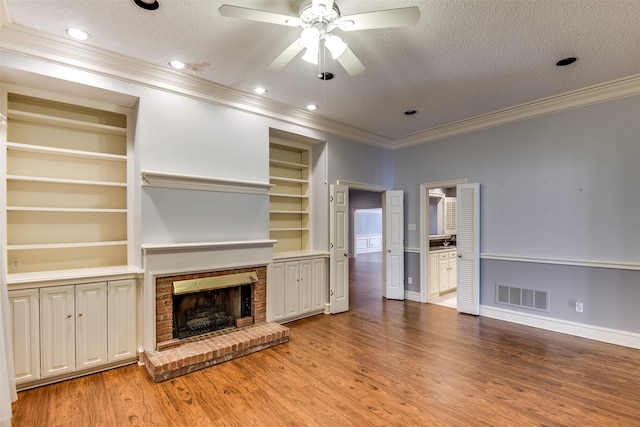 unfurnished living room with built in shelves, crown molding, light wood-type flooring, and a textured ceiling