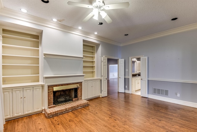 unfurnished living room with a fireplace, ornamental molding, a textured ceiling, built in shelves, and light wood-type flooring