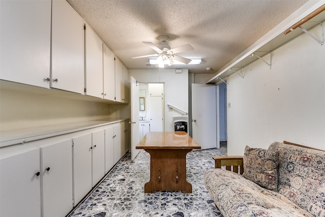 kitchen featuring ceiling fan, a kitchen island, white cabinetry, and a textured ceiling