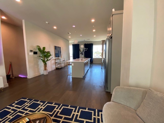 kitchen featuring stainless steel refrigerator, sink, dark hardwood / wood-style floors, a breakfast bar area, and a center island with sink