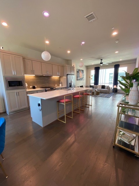 kitchen featuring hanging light fixtures, dark hardwood / wood-style flooring, stainless steel refrigerator with ice dispenser, a breakfast bar area, and a kitchen island with sink