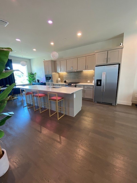 kitchen featuring a breakfast bar, an island with sink, dark hardwood / wood-style floors, and appliances with stainless steel finishes