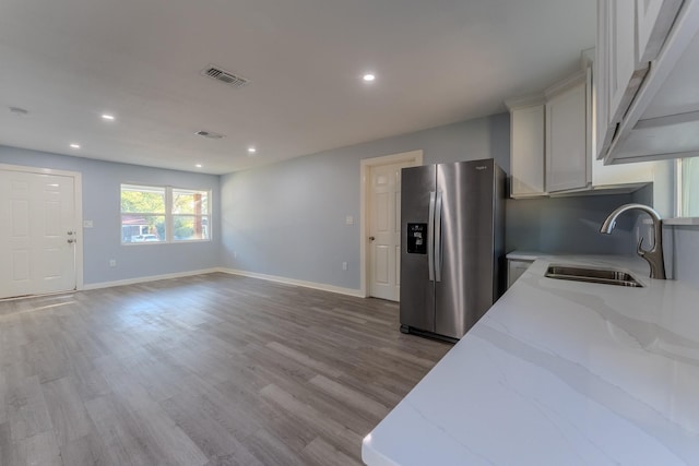 kitchen with white cabinetry, sink, light stone counters, stainless steel refrigerator with ice dispenser, and light wood-type flooring