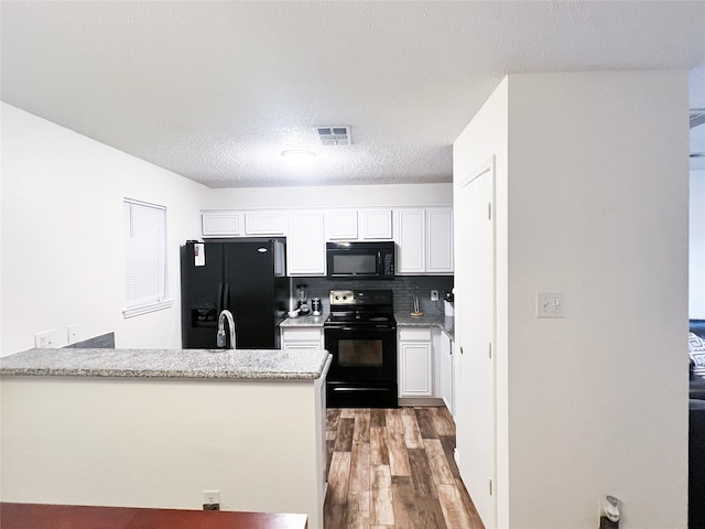 kitchen with light stone counters, dark hardwood / wood-style flooring, decorative backsplash, white cabinets, and black appliances