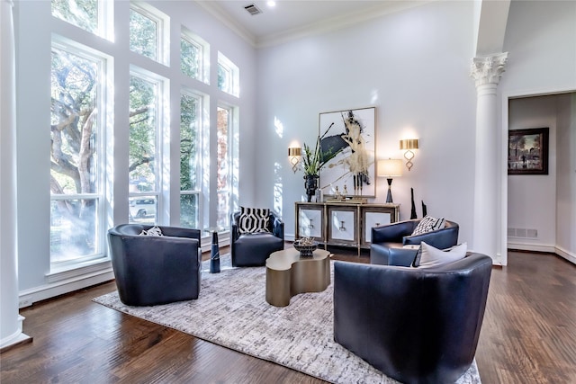 living room featuring a high ceiling, decorative columns, crown molding, and dark wood-type flooring