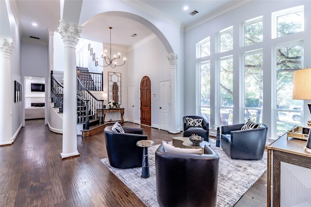 living room featuring dark wood-type flooring, a high ceiling, an inviting chandelier, ornamental molding, and ornate columns