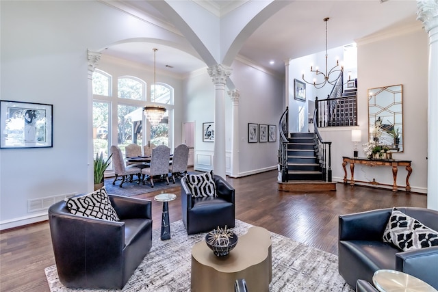 living room featuring ornate columns, wood-type flooring, crown molding, and an inviting chandelier