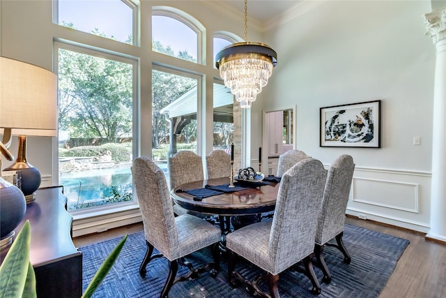 dining space featuring ornate columns, a high ceiling, an inviting chandelier, crown molding, and hardwood / wood-style flooring