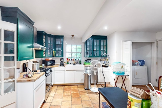 kitchen featuring butcher block counters, sink, wall chimney exhaust hood, washer / dryer, and appliances with stainless steel finishes