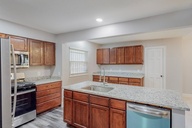 kitchen featuring appliances with stainless steel finishes, brown cabinets, light stone countertops, light wood-type flooring, and a sink