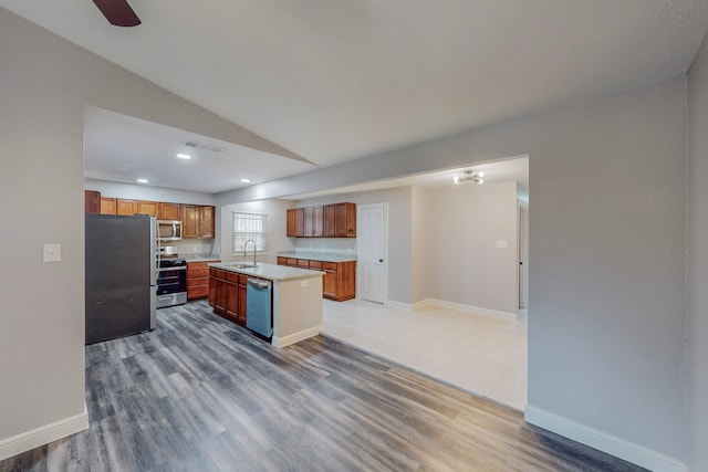 kitchen with a center island with sink, appliances with stainless steel finishes, brown cabinets, light countertops, and a sink