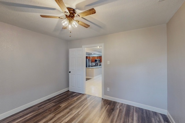 unfurnished room with ceiling fan, dark wood-style flooring, a textured ceiling, and baseboards