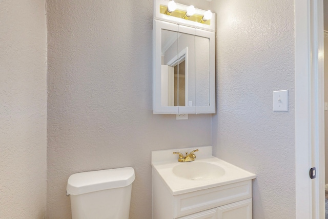 half bathroom featuring toilet, a textured wall, and vanity