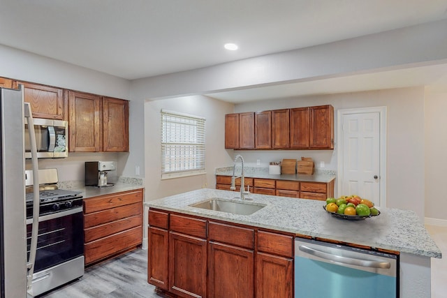 kitchen with appliances with stainless steel finishes, brown cabinets, light stone countertops, light wood-type flooring, and a sink