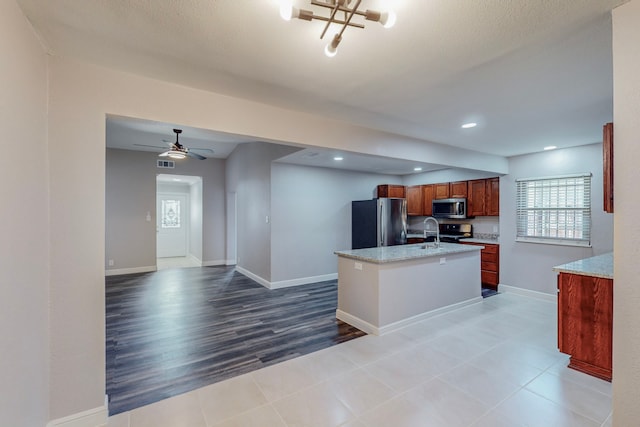 kitchen featuring a kitchen island with sink, a sink, open floor plan, appliances with stainless steel finishes, and brown cabinetry