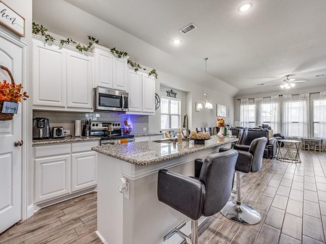 kitchen featuring stainless steel appliances, a kitchen island with sink, white cabinets, ceiling fan with notable chandelier, and light wood-type flooring