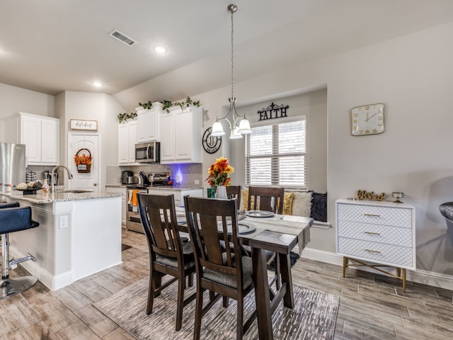 dining area featuring sink, an inviting chandelier, vaulted ceiling, and light wood-type flooring