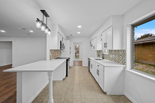 kitchen with appliances with stainless steel finishes, a kitchen breakfast bar, sink, decorative light fixtures, and white cabinets