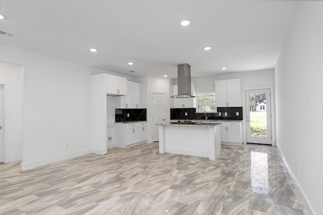 kitchen with white cabinetry, a center island, wall chimney exhaust hood, light stone countertops, and backsplash