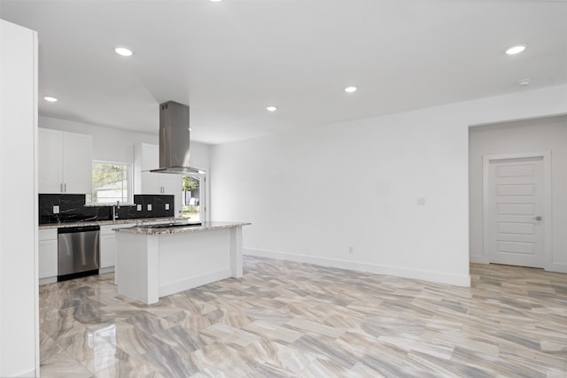 kitchen featuring light stone countertops, wall chimney exhaust hood, a kitchen island, stainless steel dishwasher, and white cabinets