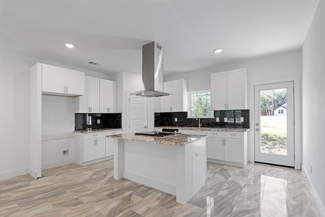 kitchen with a center island, white cabinets, decorative backsplash, light stone countertops, and island range hood