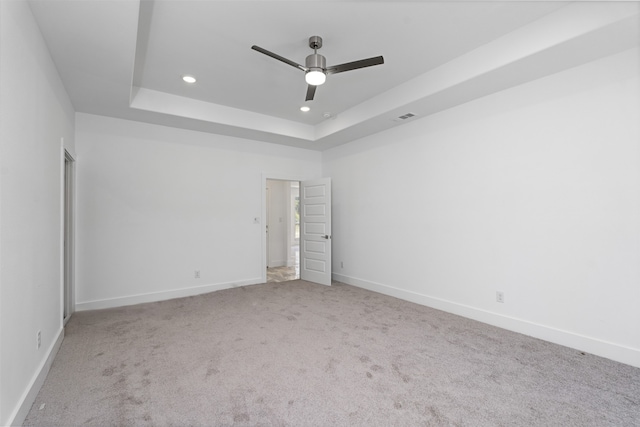 spare room featuring light carpet, a tray ceiling, and ceiling fan